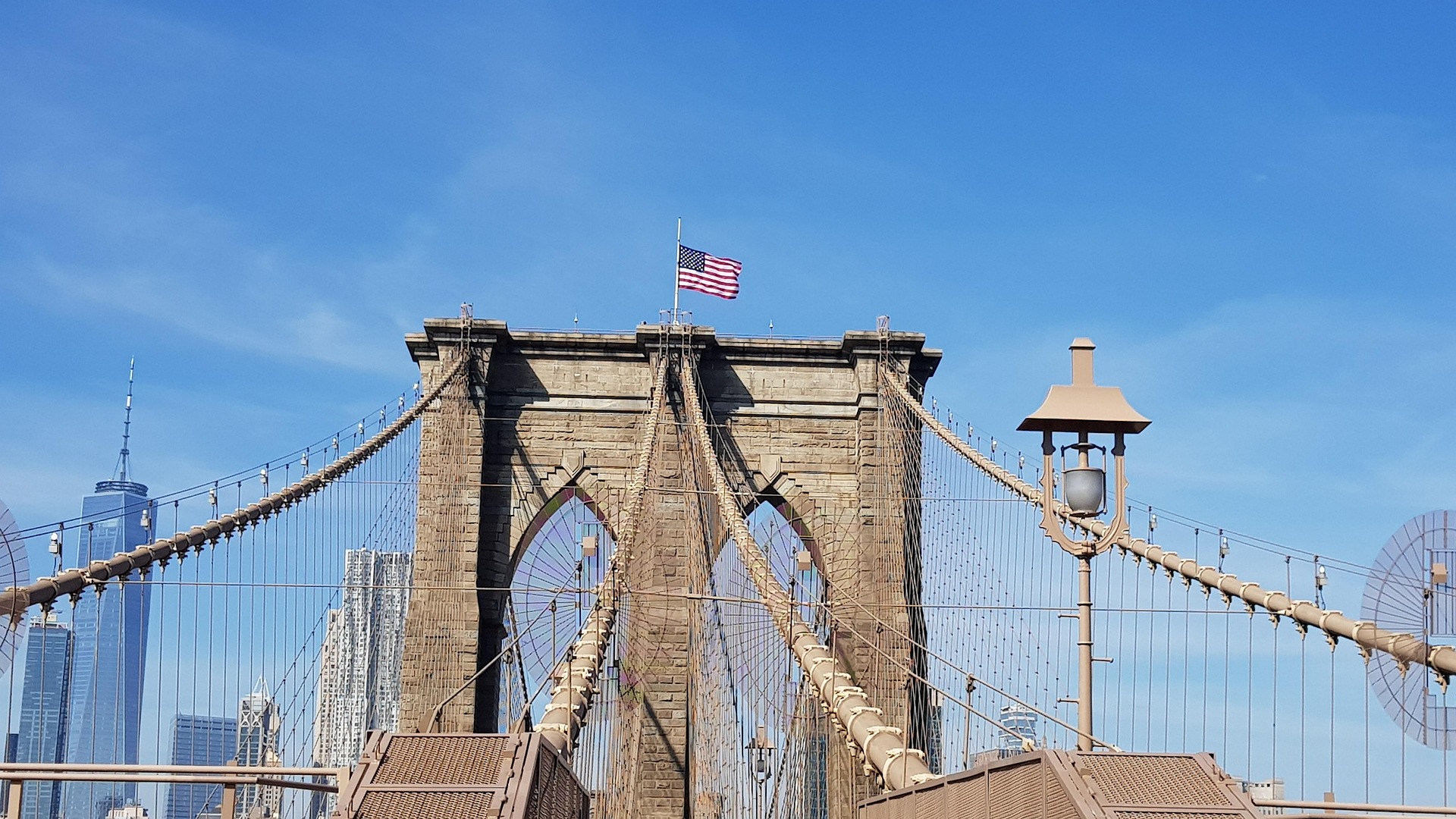 Americká vlajka na mostu Brooklyn Bridge vlaje na modré obloze nad řekou East River.