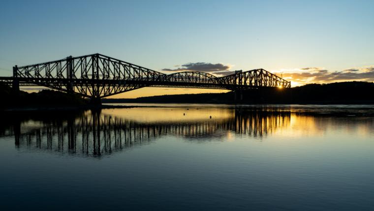 Die Québec-Brücke ragt majestätisch in der Morgendämmerung in den Himmel und spiegelt sich im stillen Wasser wider.