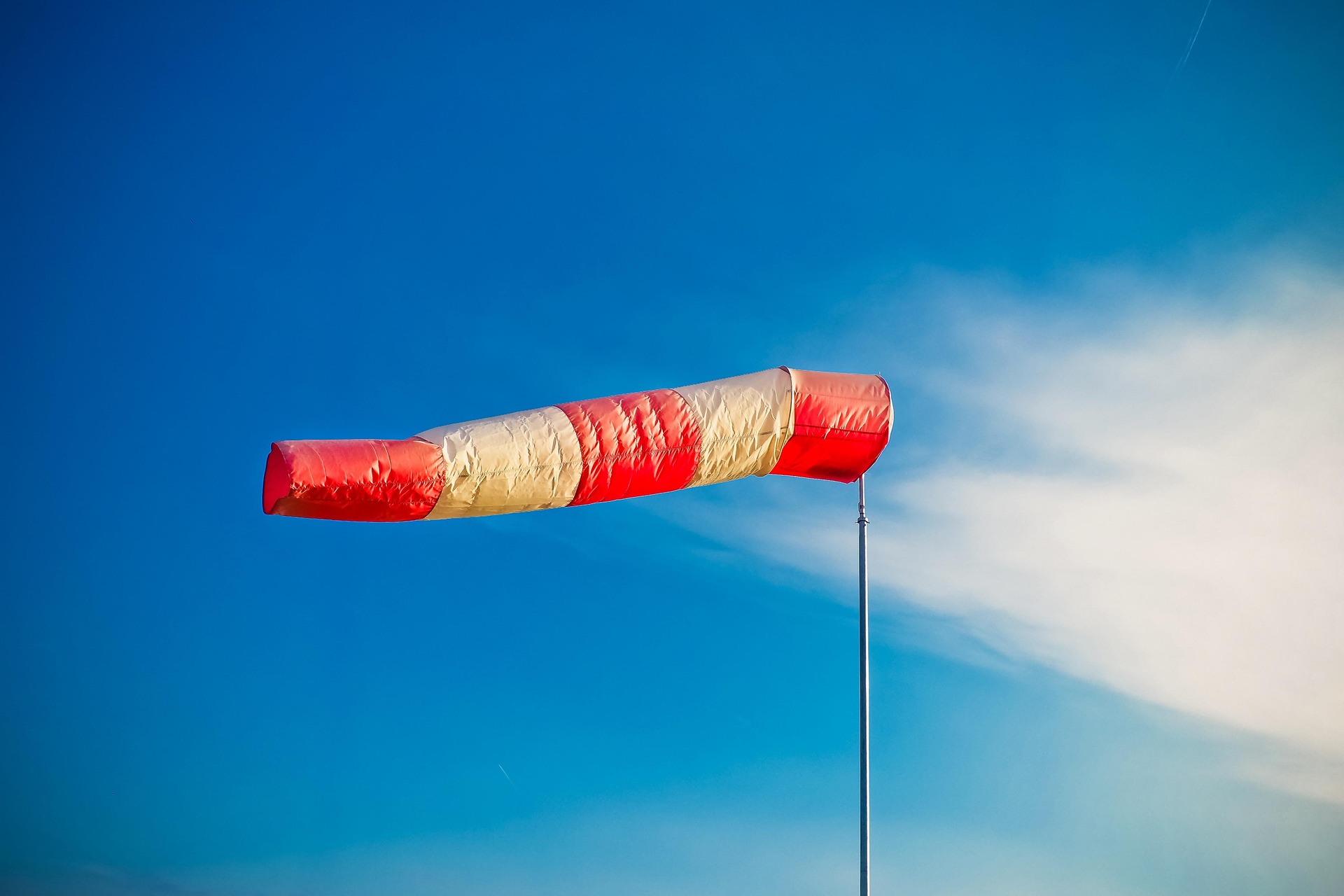 Ein rot-weißer Windsack an einem Mast vor blauem Himmel visualisiert die Notwendigkeit der Berücksichtigung von Windlasten und Böen bei der statischen Berechnung von Bauwerken