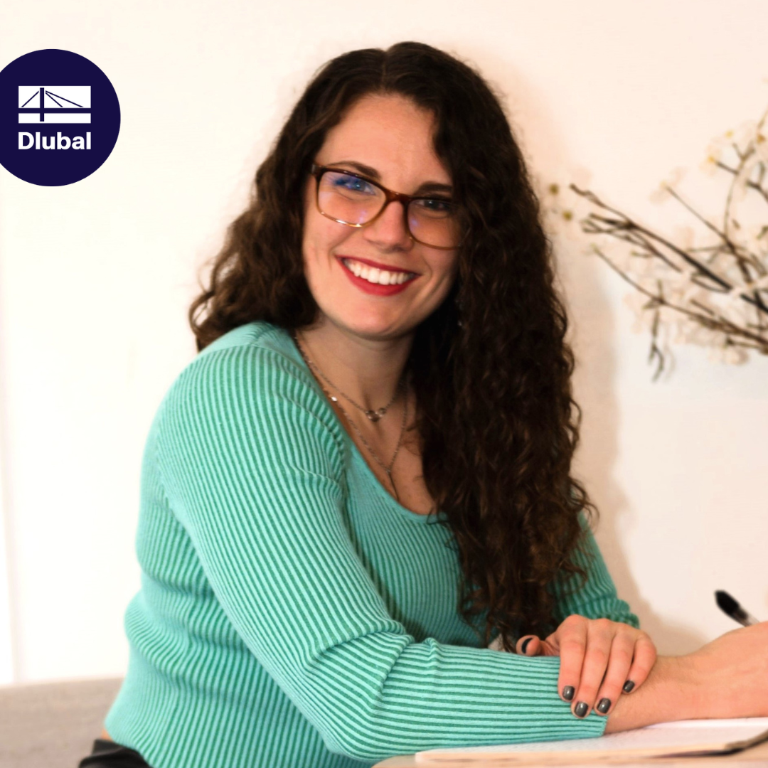 Katie, the new colleague, smiles at the camera and wears office clothes.