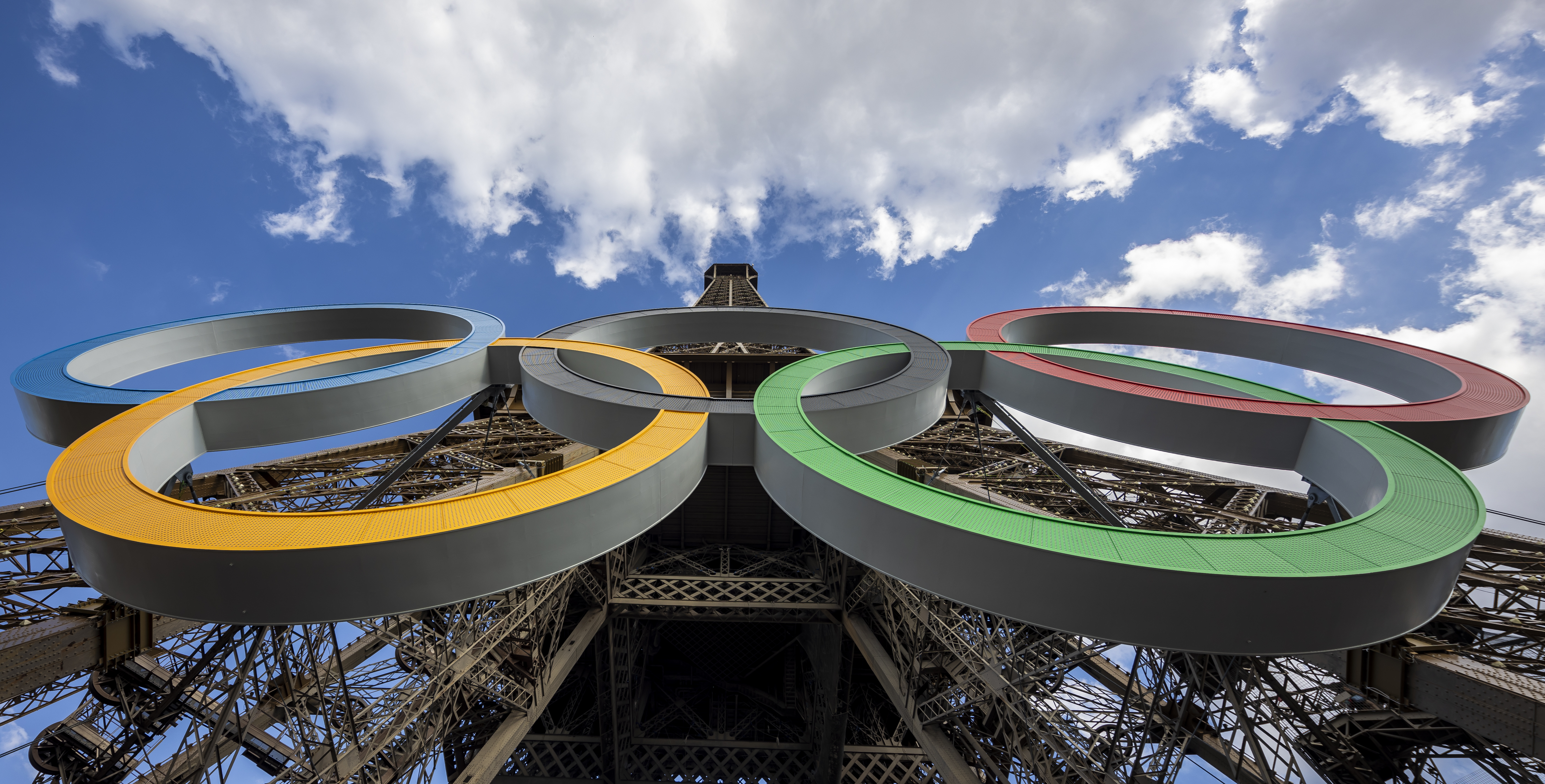 Primer plano de los cinco aros olímpicos en la Torre Eiffel bajo un cielo azul