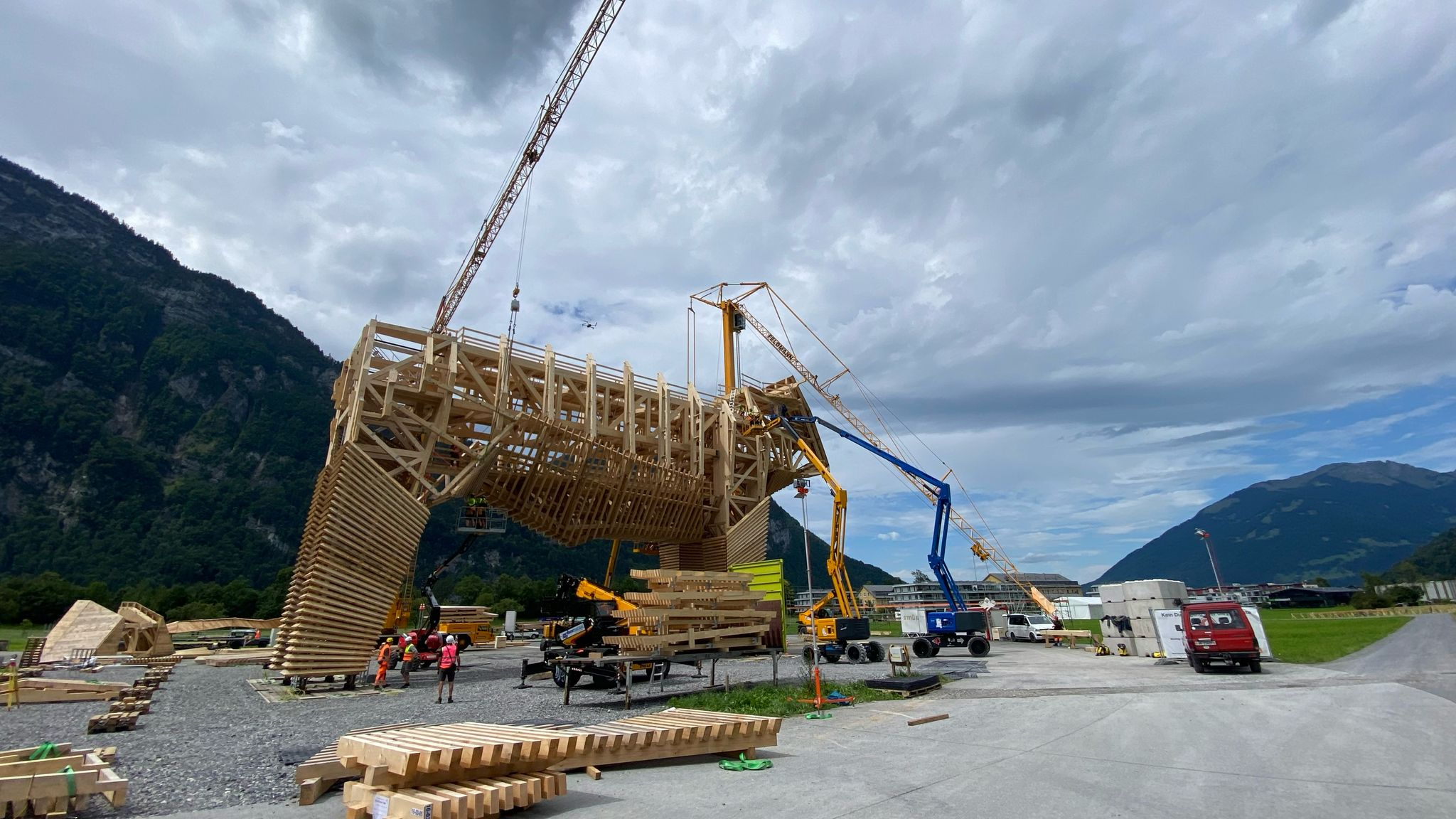 Montaggio della struttura in legno del toro in legno con gru edile, configurazione con gru telescopica e piattaforme elevabili sull'area di montaggio davanti a uno sfondo montuoso