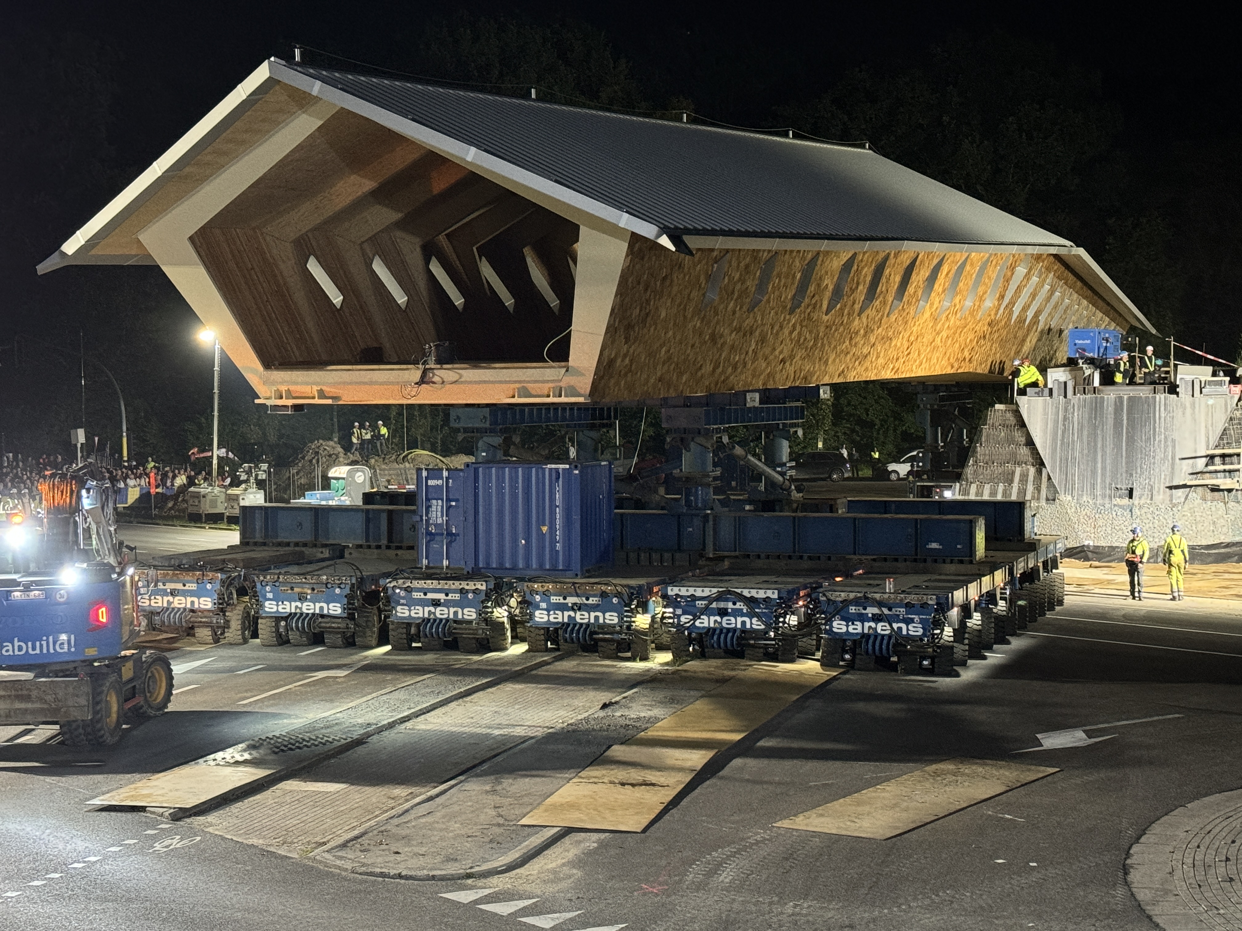 Trasporto notturno di un ponte ibrido legno-legno per ciclisti e pedonali su trasportatori modulari semoventi della ditta Sarens a Bruxelles