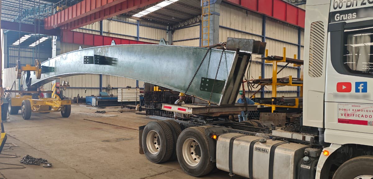 Łukowa belka stalowa mostu podnoszona i ładowana suwnicami na samochód transportowy w warsztacie produkcji metalowej.