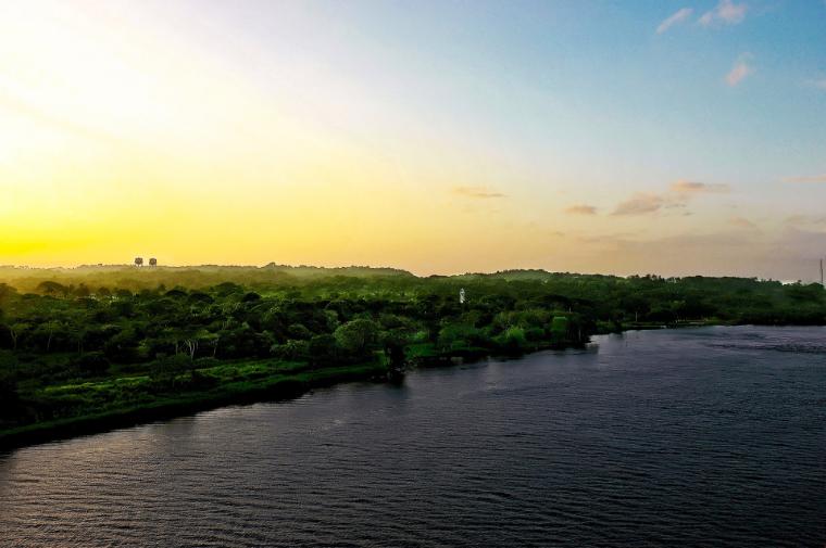 Paisagem vasta com vegetação e corpo de água ao longo do Canal do Panamá, rodeada por colinas verdes e árvores