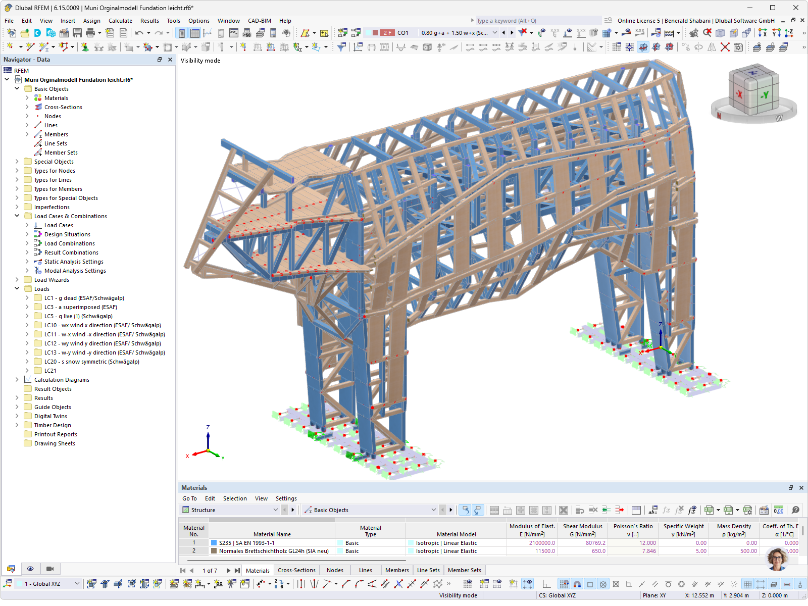 Modelo 3D detalhado em elementos finitos de um pórtico de madeira no software RFEM, mostrando a complexa estrutura de treliça, pilares, vigas transversais e a fundação subjacente. O modelo inclui vários casos de carga, como peso próprio, vento e neve, bem como a definição de materiais de madeira para o cálculo estrutural.