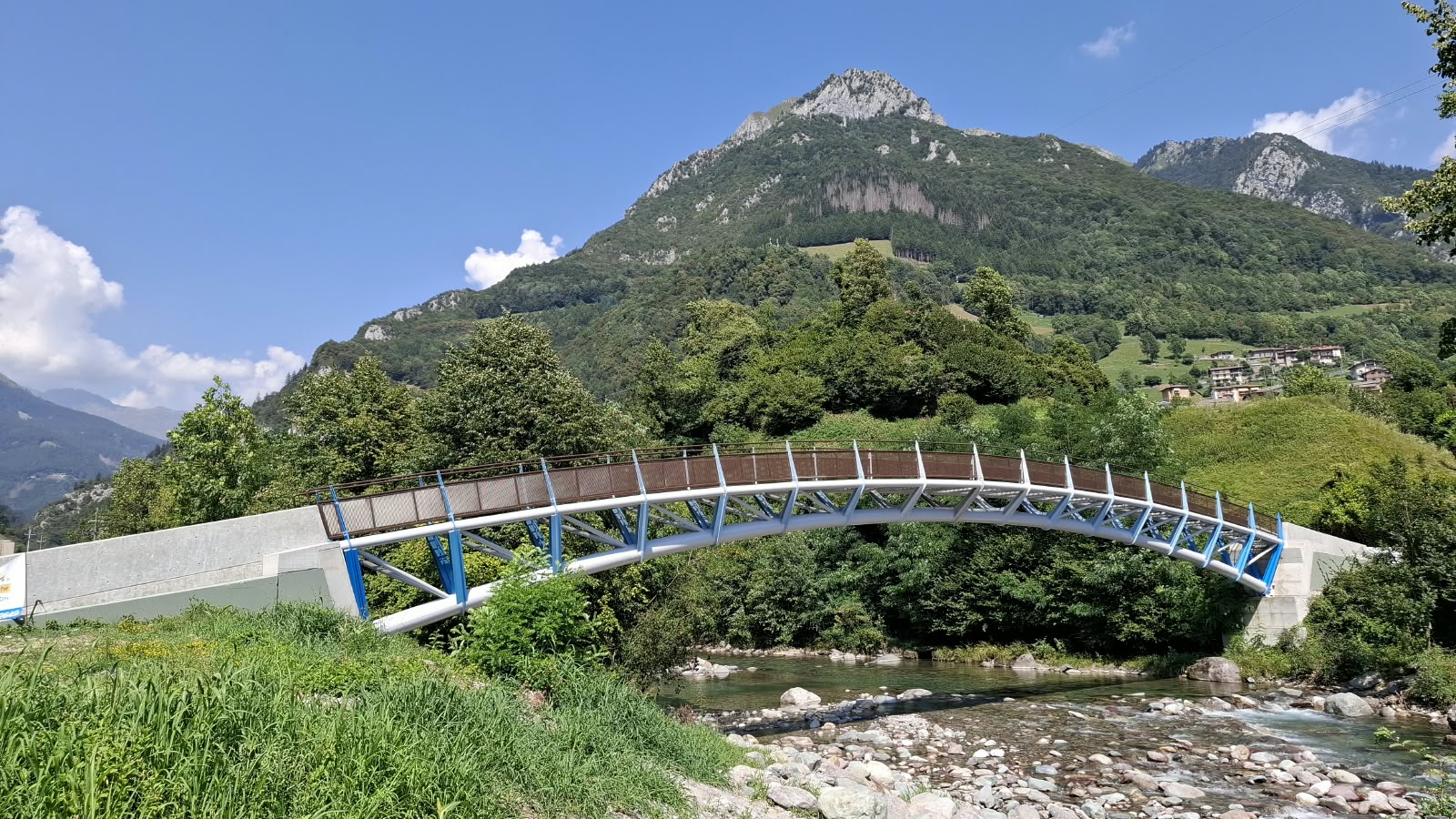 Ponte curva para peões em aço sobre um rio em frente a uma paisagem montanhosa alpina em Itália