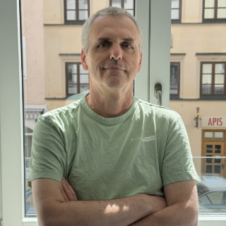 Сотрудник команды Dlubal стоит перед офисными окнами, скрестив руки, с дружелюбным выражением лица.